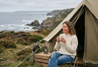 Femme en pull écru assise devant une tente de camping sur une falaise bretonne face à l'océan Atlantique