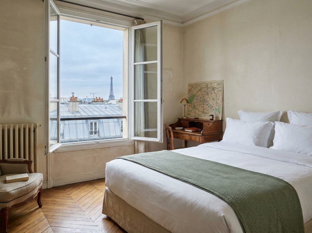 Chambre d'hôtel parisienne avec vue sur les toits et la Tour Eiffel au loin, parquet en chevrons et linge blanc